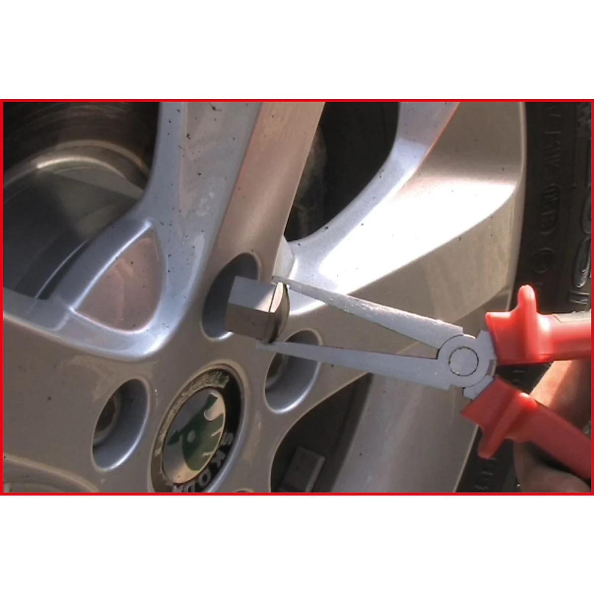 Nahaufnahme: Zange an einem silbernen Autoreifen, der ein Radmutter herausnimmt.